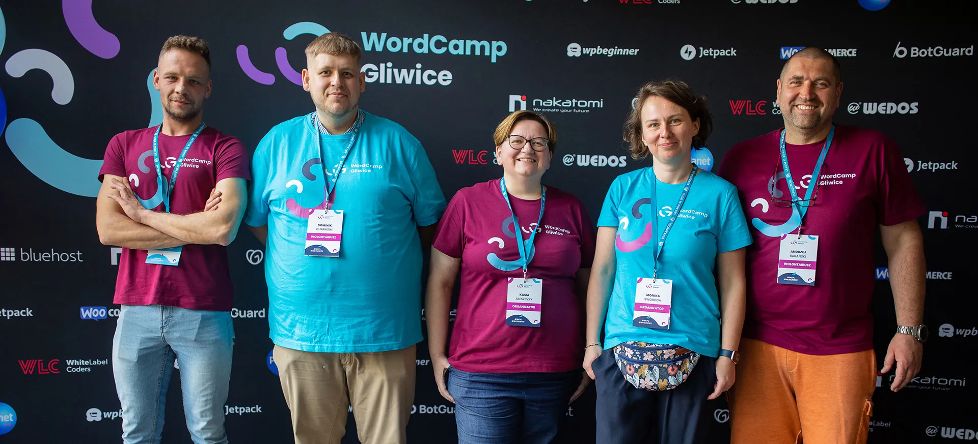 WordCamp Gliwice 2024 organizers and volunteers in front of the sponsor wall